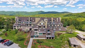 A multi-story hotel with a central clock tower, surrounded by lush greenery and mountains in the background. - Mountain Green Resort By Killington VR - 3 Bedrooms (Killington)