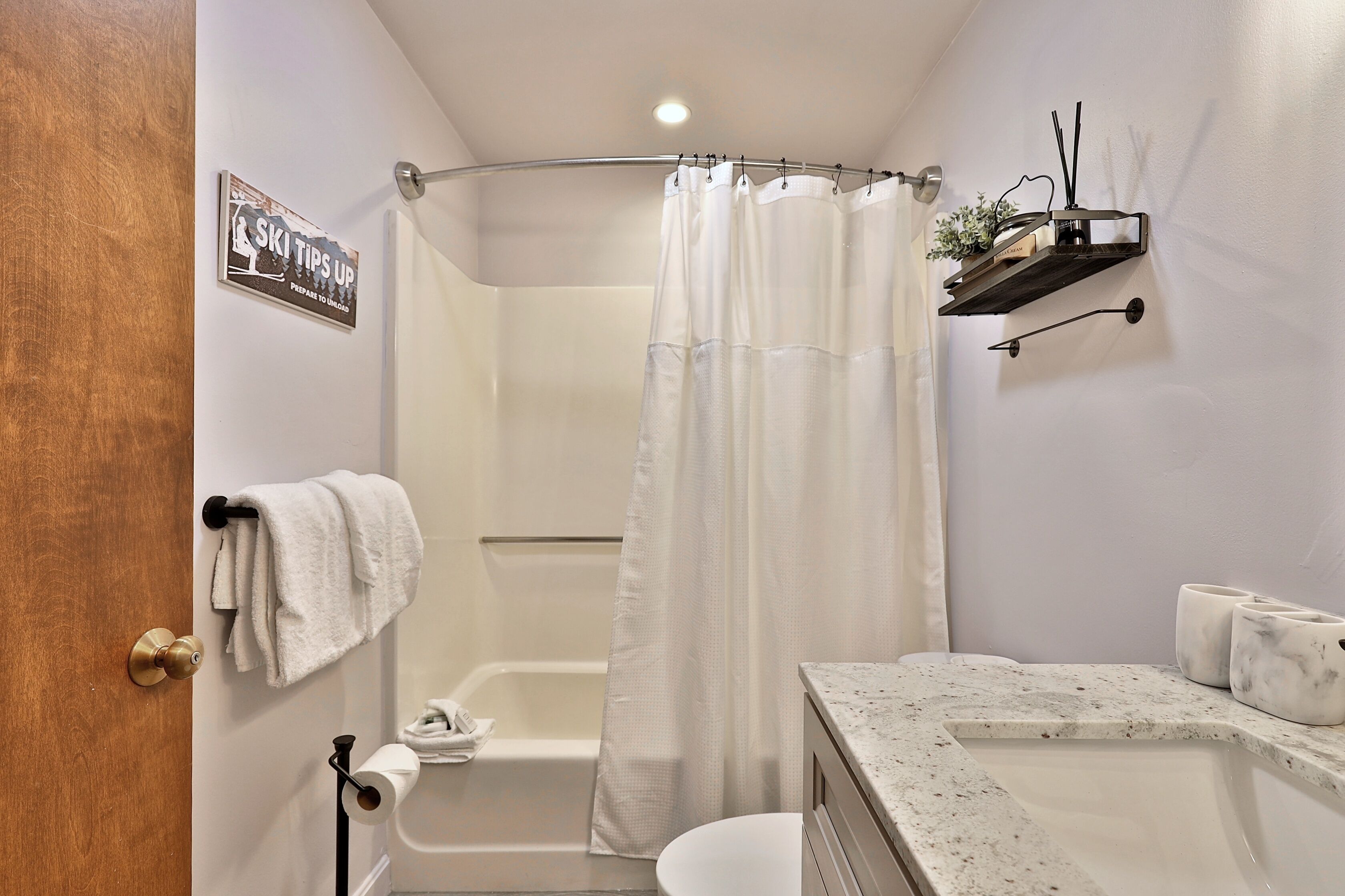 A bathroom with a shower curtain, a towel rack, a toilet, and a sink with a marble countertop.
