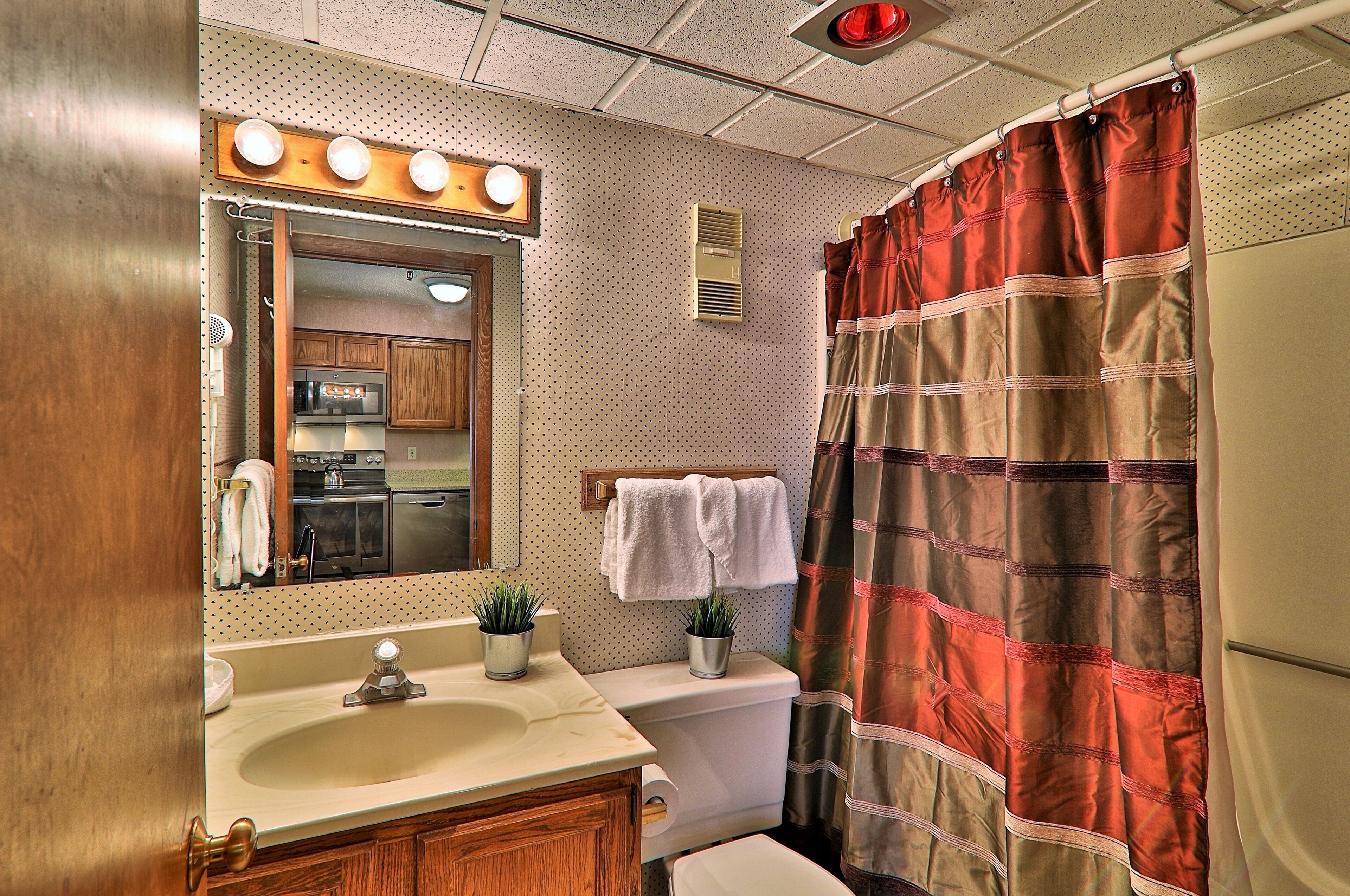 A bathroom with a sink, mirror, toilet, and shower curtain.