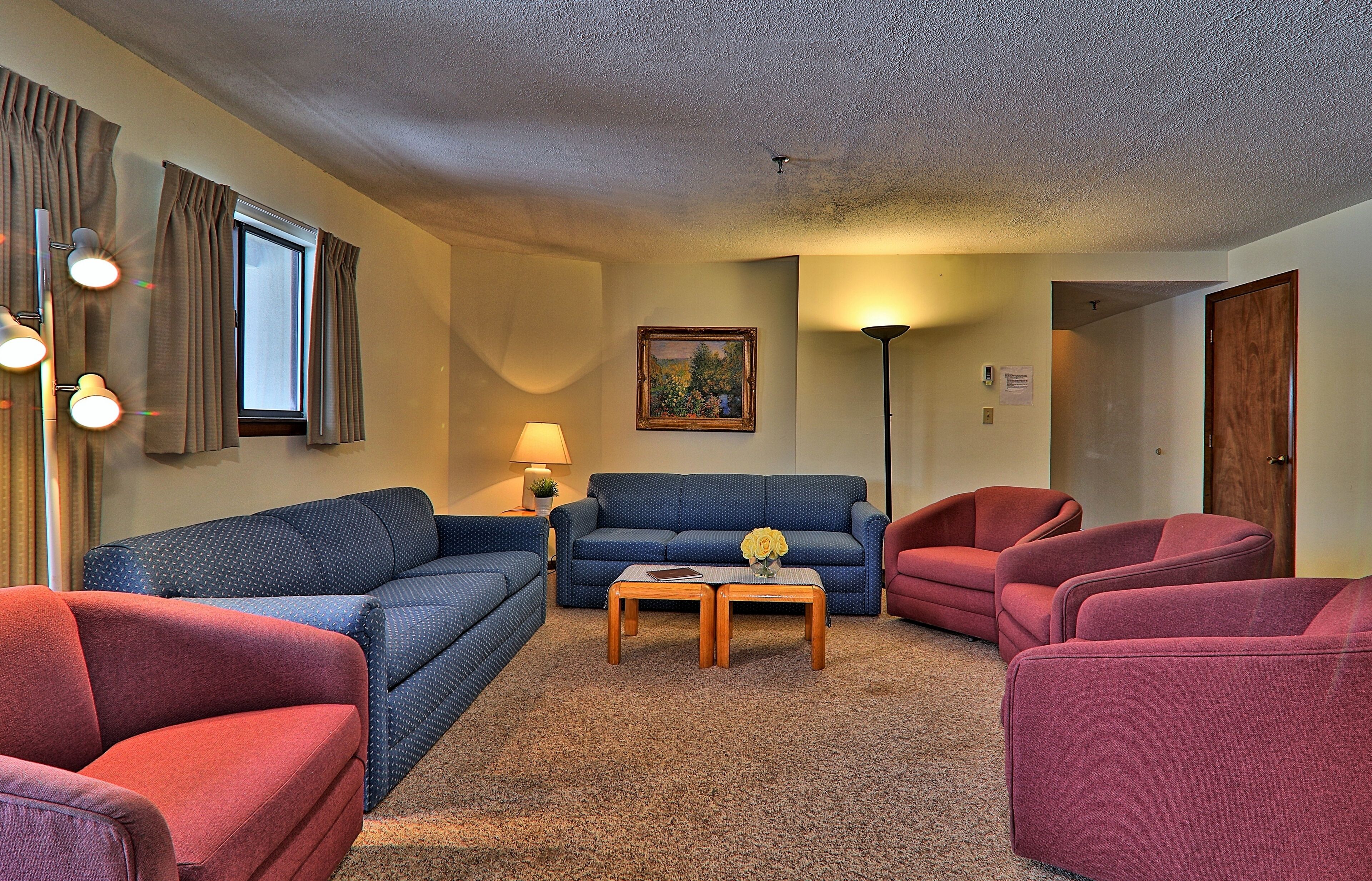 A living room with a blue sofa, red armchairs, a wooden coffee table, and a lamp.