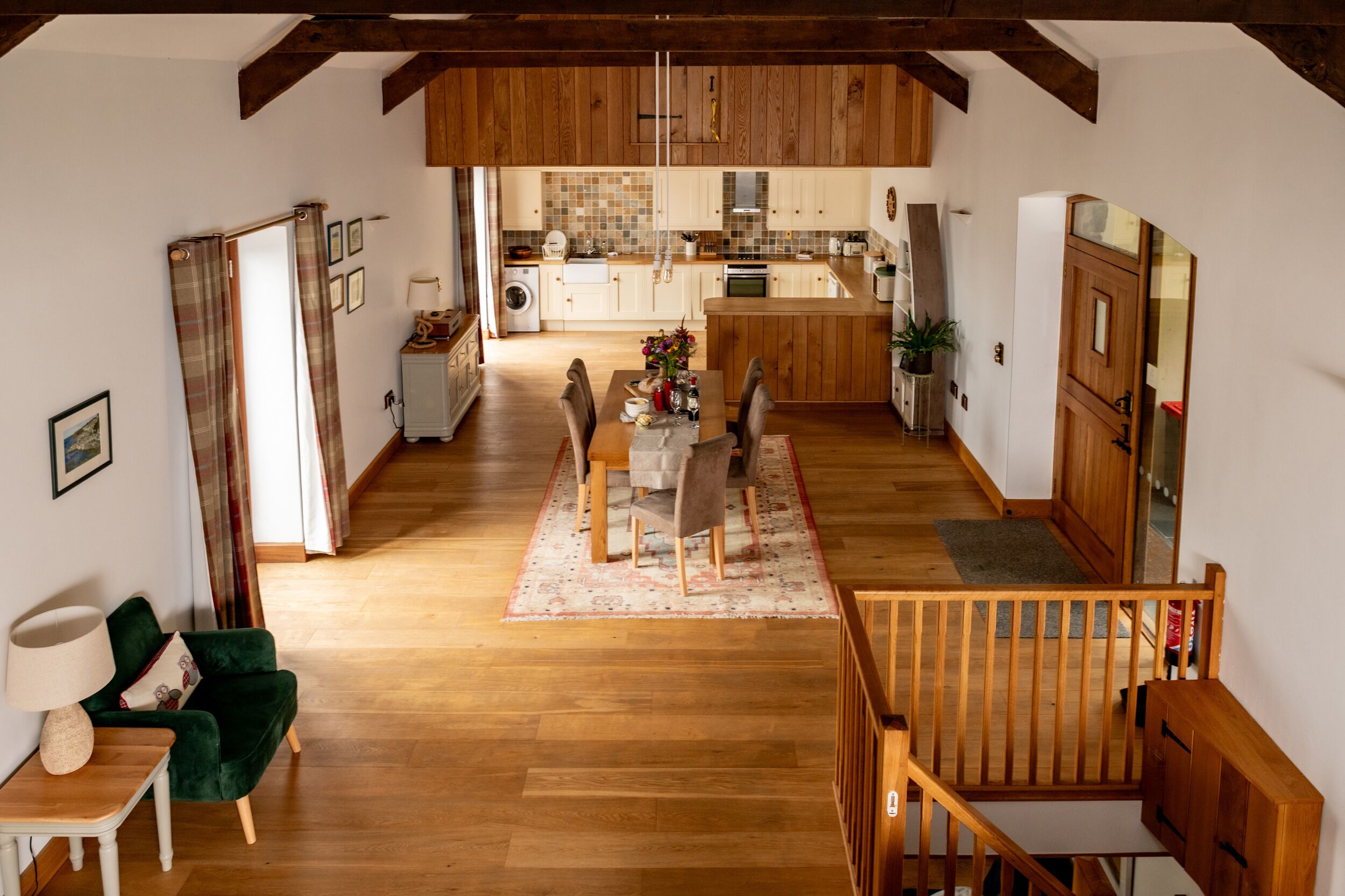 Una habitación amplia con piso de madera, un área de comedor con mesa y sillas, un sillón verde y una escalera que sube a un nivel superior.