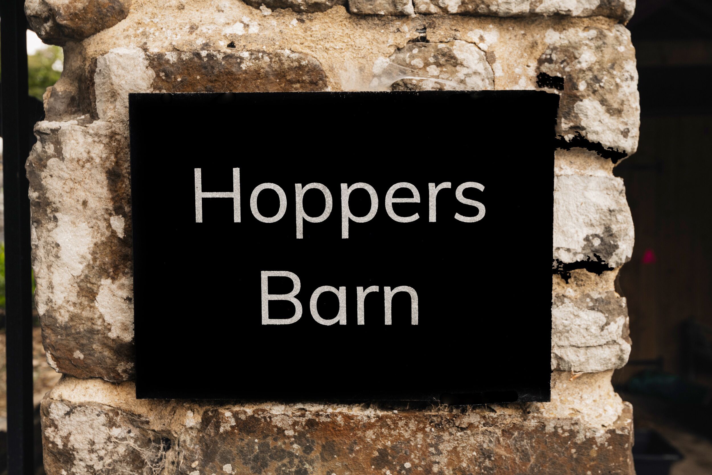 A black sign with white lettering on a stone wall, reading 'Hoppers Barn.'