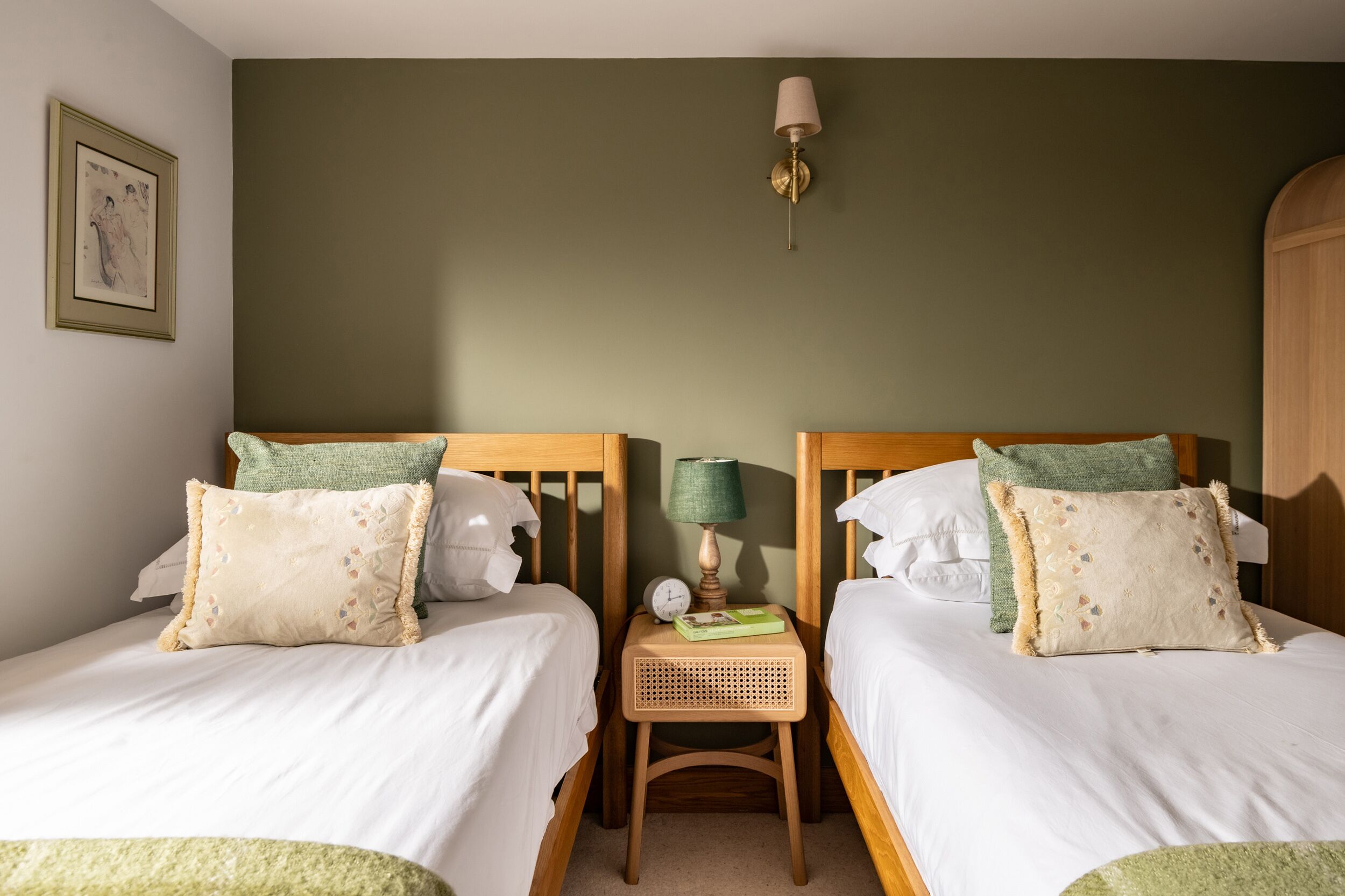 Een slaapkamer met twee eenpersoonsbedden, een klein houten nachtkastje met een lamp en een lijst met een afbeelding aan de muur.