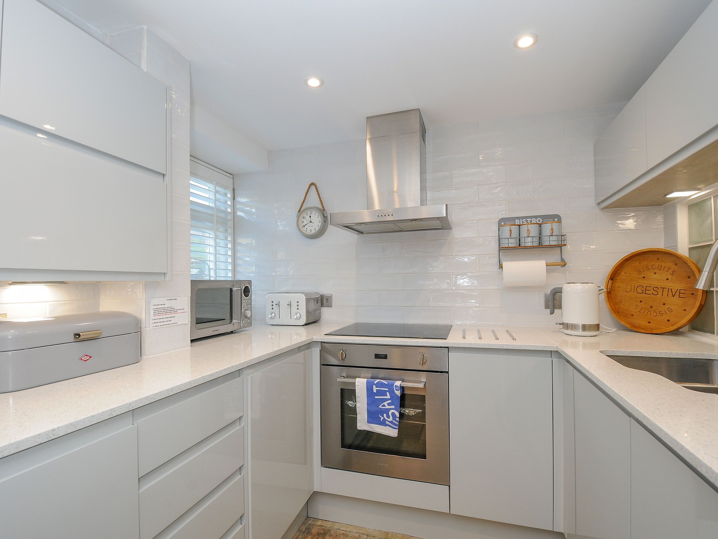 Una cocina moderna con armarios blancos, una campana extractora de acero inoxidable, un microondas, un tostador y una tabla de cortar de madera con la palabra 'DIGESTIVE'.