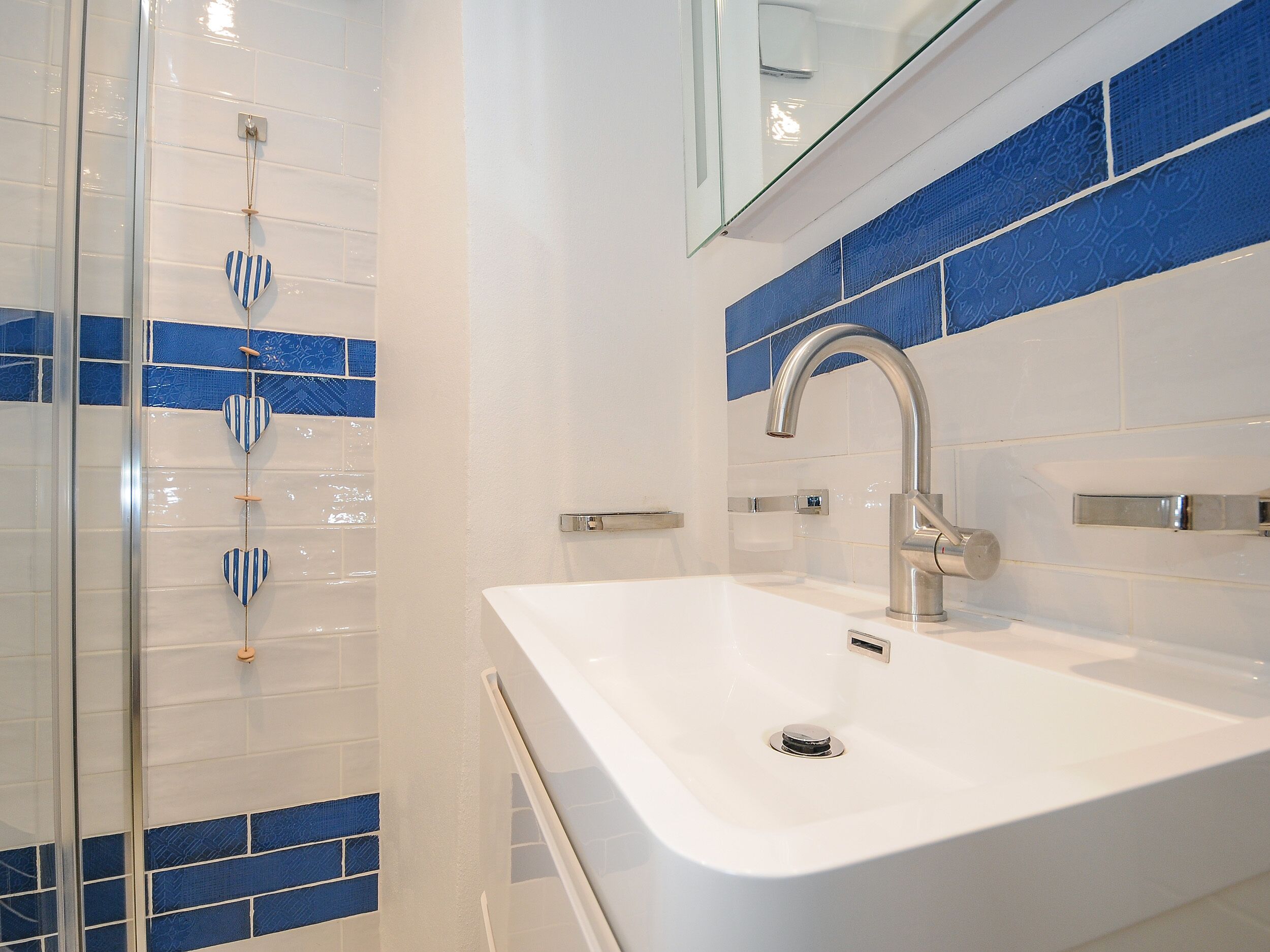 Un baño moderno con un lavamanos blanco, un grifo cromado y paredes con azulejos azules.