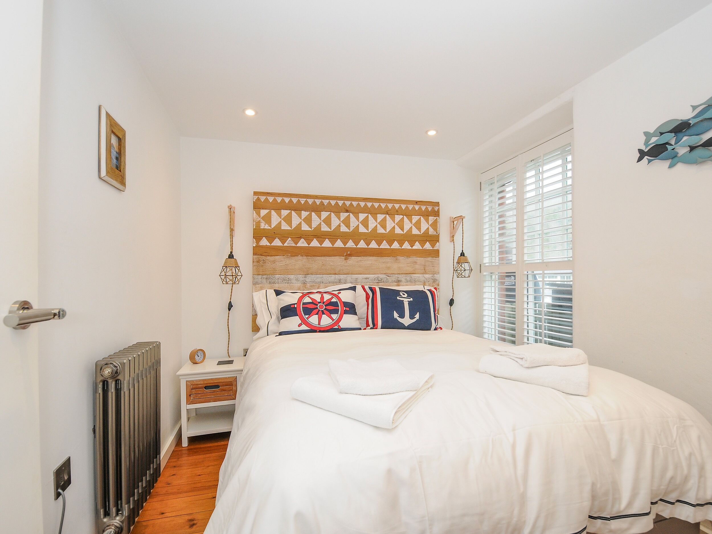 Une chambre à coucher avec une tête de lit en bois, un lit avec une literie blanche, une table de chevet avec une lampe et une fenêtre avec des stores.
