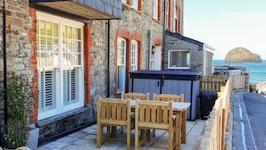 A coastal building with a stone facade, wooden outdoor seating, and a view of the sea. - Salty Sea Dog (Tintagel)