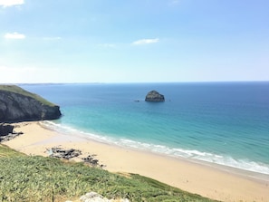 A coastal landscape with a sandy beach, a rocky outcrop, and calm sea.