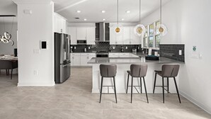 A modern kitchen with a central island, bar stools, and pendant lighting.