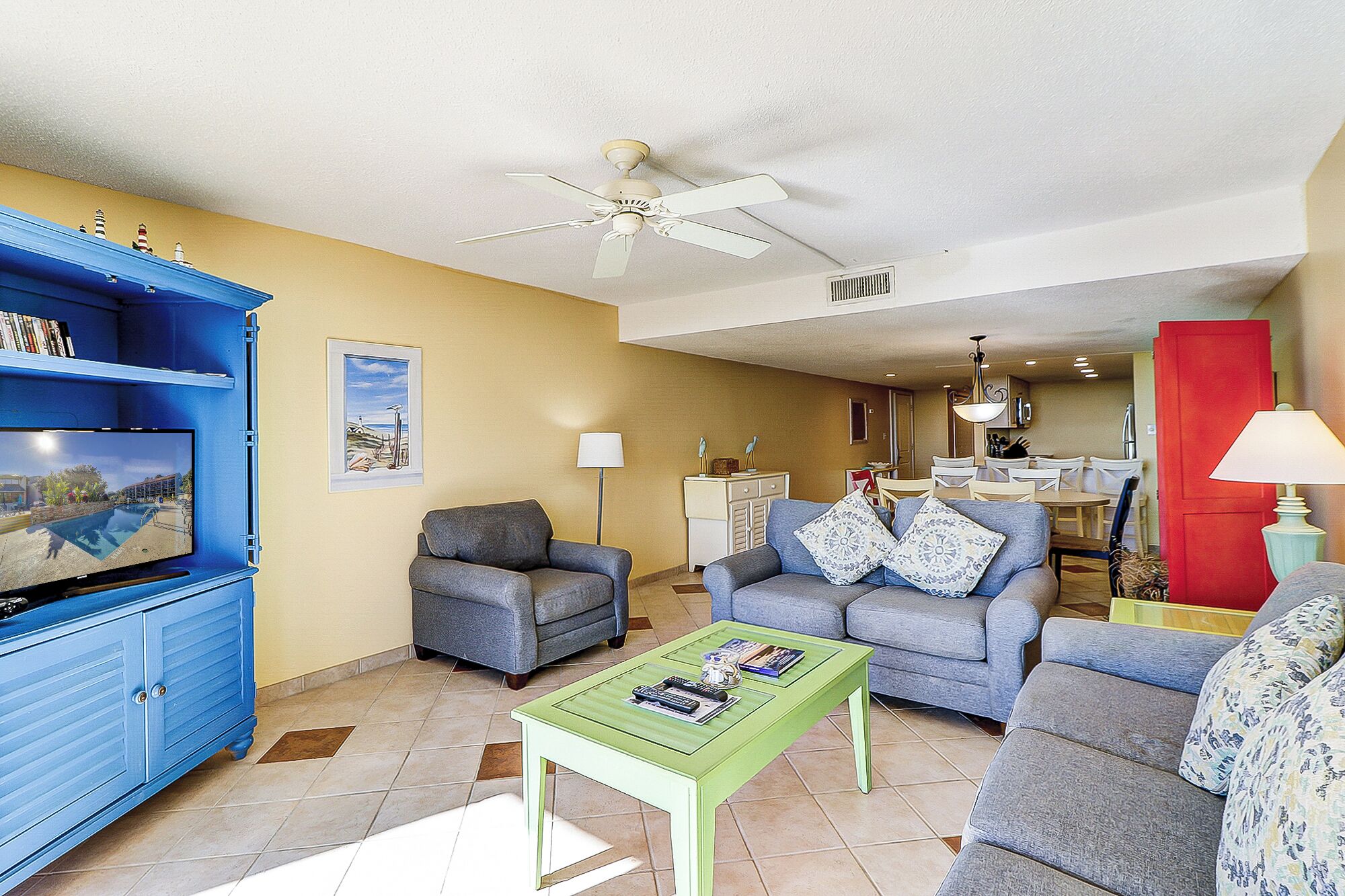 A living room with a blue entertainment unit, two grey sofas, a green coffee table, and a ceiling fan.