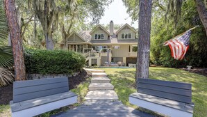 Un chemin menant à une maison avec une piscine, entourée d’arbres et sur laquelle flotte un drapeau américain.