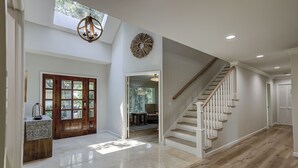 Un intérieur spacieux agrémenté d’un escalier en bois, d’une grande porte en bois et d’un lustre.