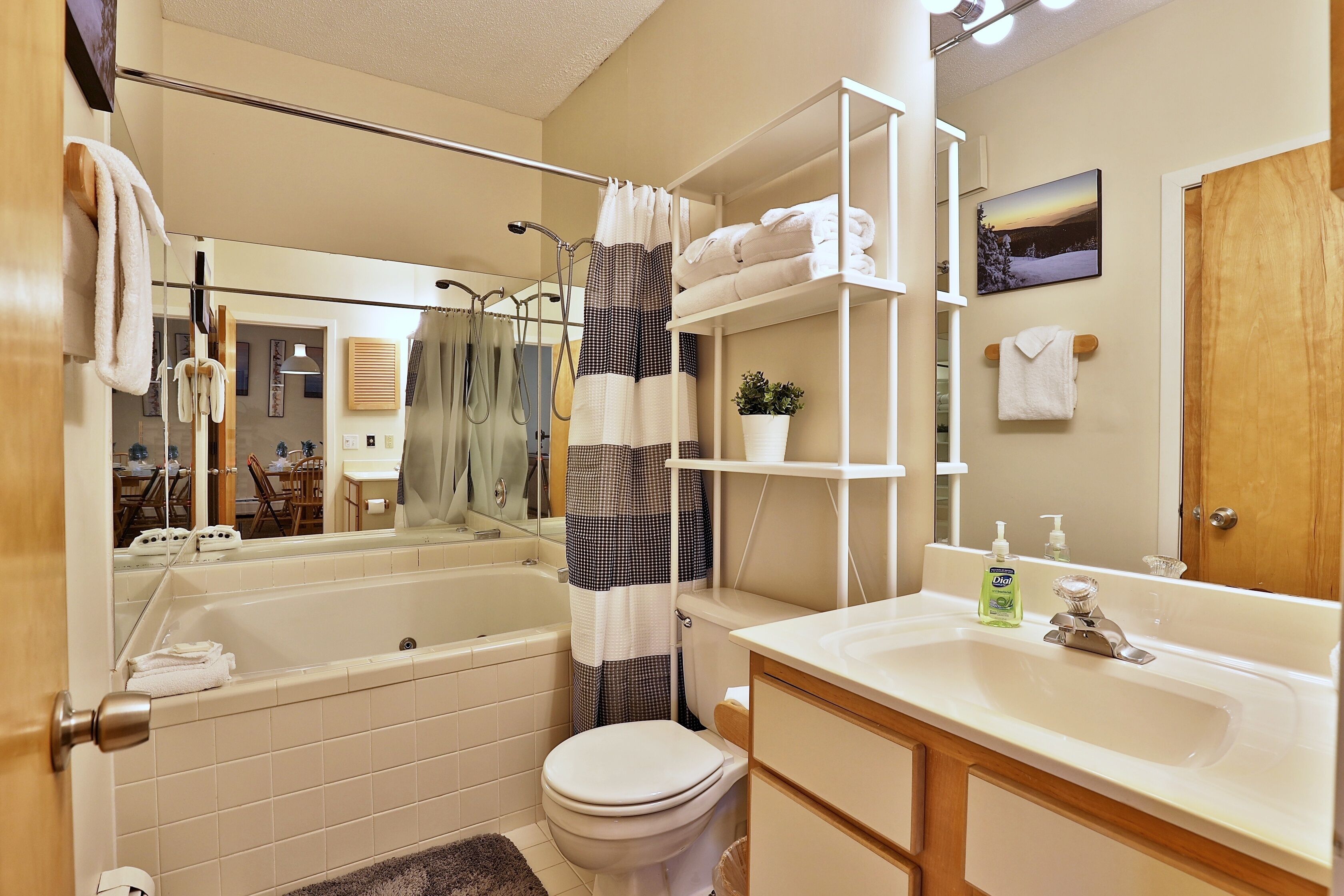 A bathroom with a bathtub, toilet, and sink. There are towels and a plant on shelves.