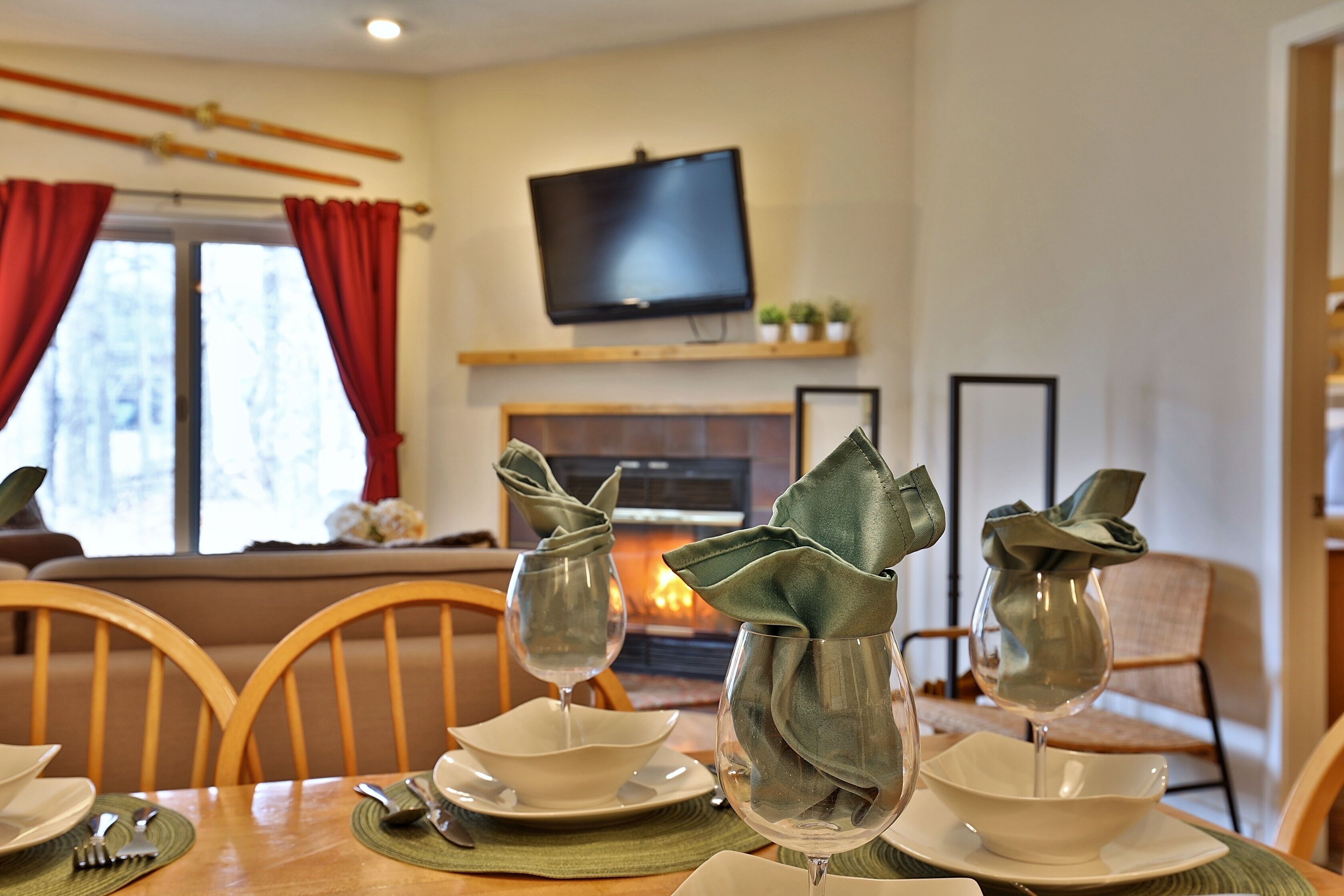 A dining table set with plates, cutlery, and wine glasses, with a fireplace and television in the background.