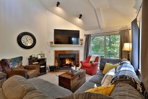 Ein Wohnzimmer mit Kamin, Fernseher und einem großen Fenster mit Vorhängen.