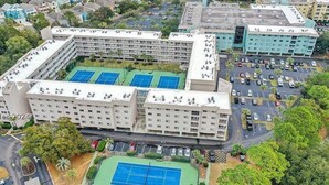 A multi-story hotel with several tennis courts and a parking area. - Snow Lion On The Beach 2 Bedroom Villa by RedAwning (Hilton Head Island)