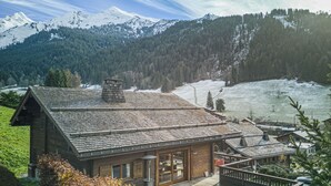 A wooden cabin with a deck, large windows, and a view of snow-covered mountains. - Cosy family chalet. Privileged location (La Clusaz)