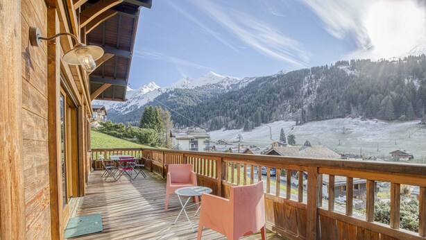 A wooden deck with two chairs and a table, overlooking a snowy mountain landscape. - Cosy family chalet. Privileged location (La Clusaz)