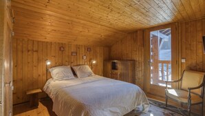 A wooden cabin bedroom with a bed, a nightstand, a wardrobe, and a chair. - Cosy family chalet. Privileged location (La Clusaz)