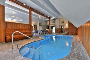 Una piscina interior con revestimiento de madera, una escalera metálica y un techo con conductos a la vista.