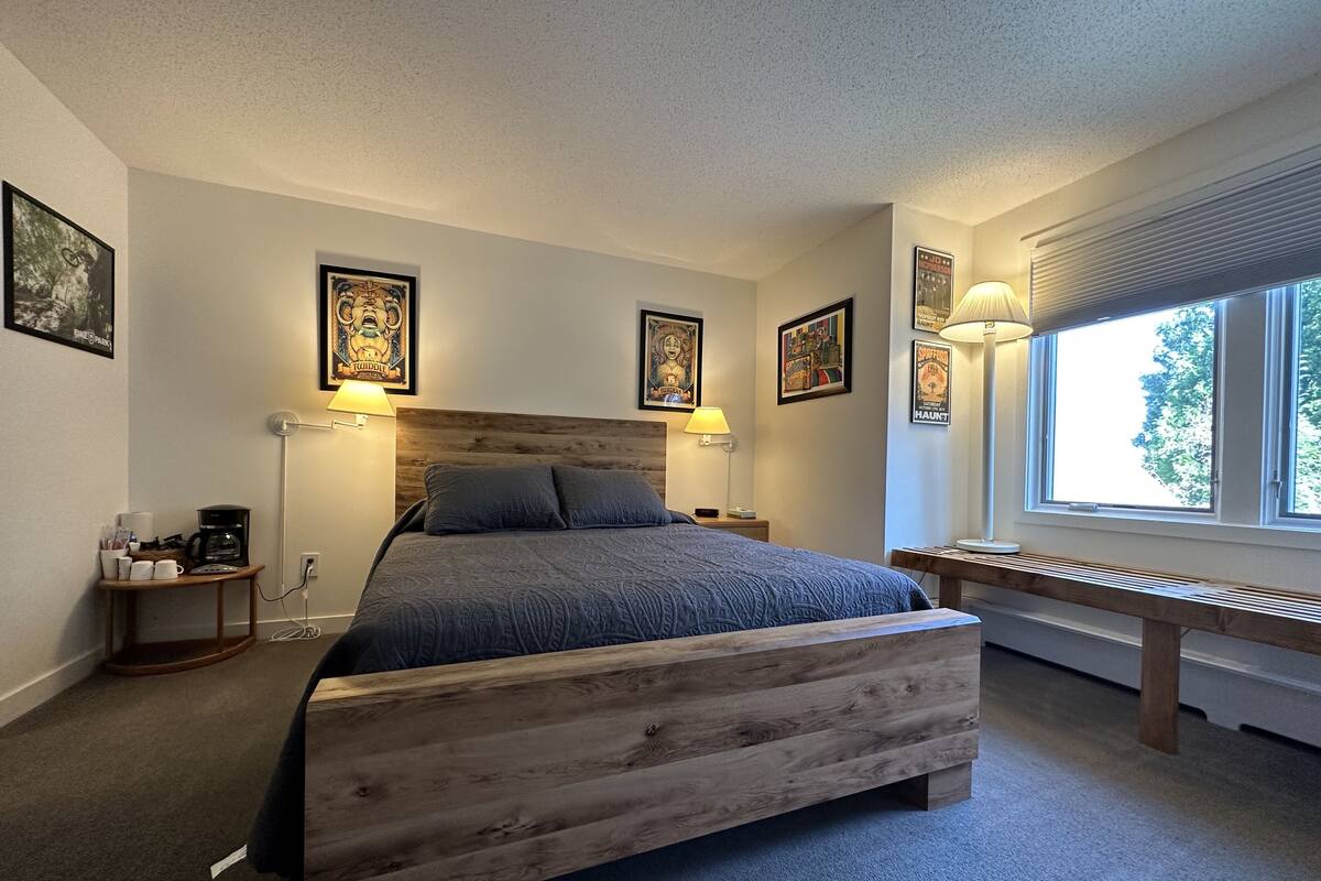 A bedroom with a wooden bed, a bedside table with a lamp, and framed artwork on the walls.
