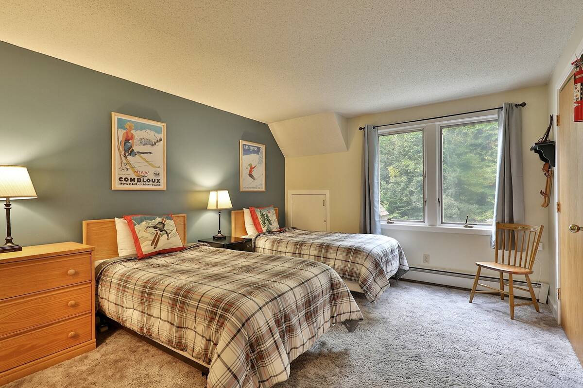 A bedroom with two beds, a dresser, a chair, and a window with a view of trees.