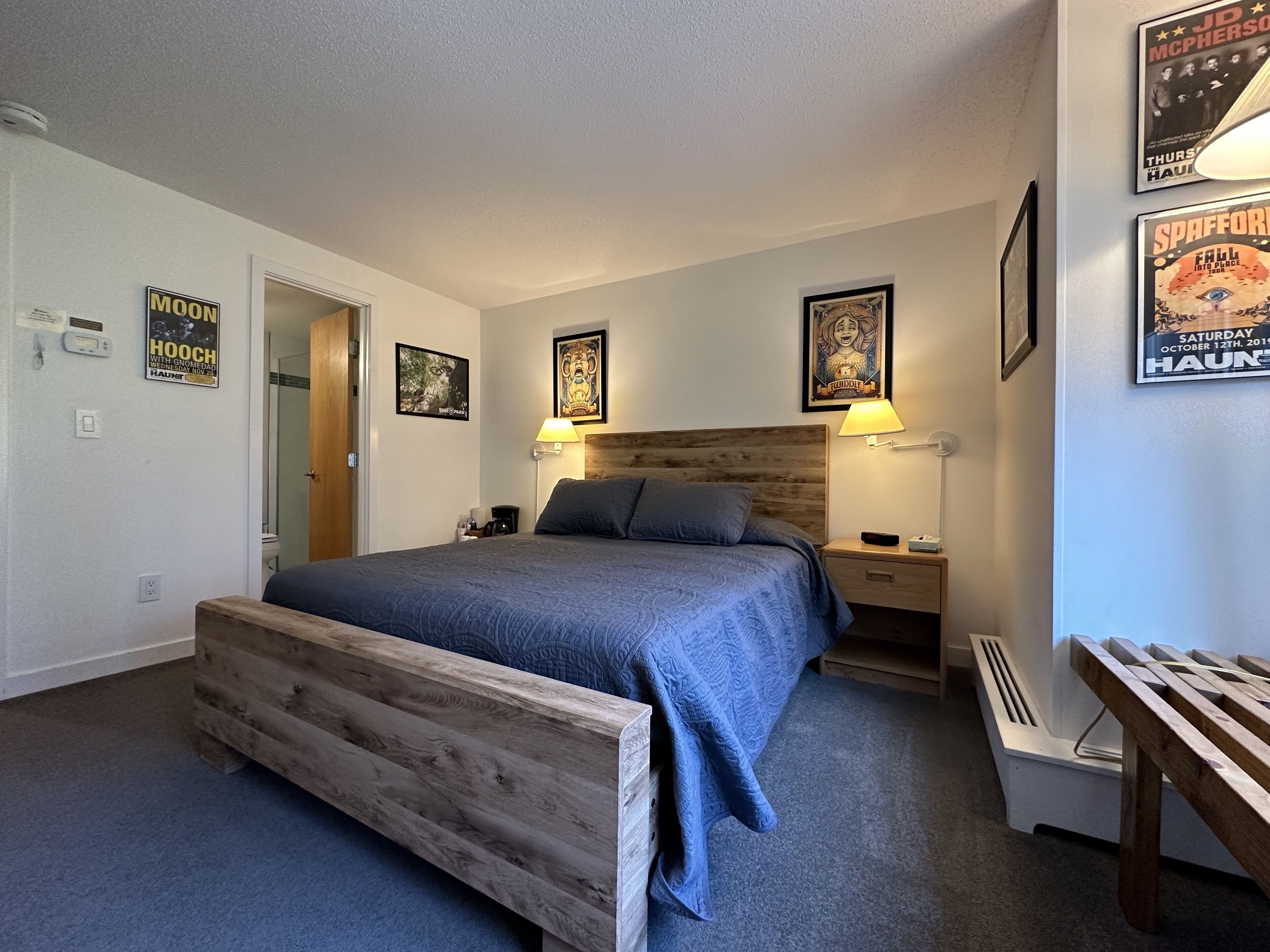Ein Schlafzimmer mit einem Bettgestell aus Holz, einer blauen Bettdecke, zwei Nachttischlampen und Postern an den Wänden.