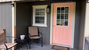 Varanda com duas cadeiras, uma mesa e uma porta rosa com a placa "FARMHOUSE".