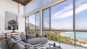 A modern living room with a large window overlooking a scenic coastal view. - Villa Anushka – Luxury 6BR Koh Samui Villa with Staff, Breakfast & Sea Views (koh samui)