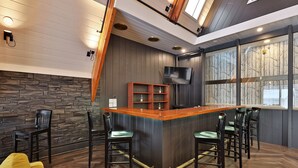 A modern bar area with a wooden counter, bar stools, and a TV mounted on the wall. - Rent An Inn! Takeover The Birch Ridge W/ Your Group. Mountain Lodge: 11 Rooms, Bar, Fireplace. 28ppl 11 Bedroom Home (Killington)