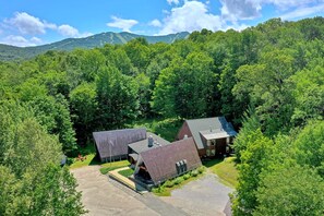 A two-story building with a sloped roof, surrounded by dense green forest and mountains in the background. - Rent An Inn! Takeover The Birch Ridge W/ Your Group. Mountain Lodge: 11 Rooms, Bar, Fireplace. 28ppl 11 Bedroom Home (Killington)
