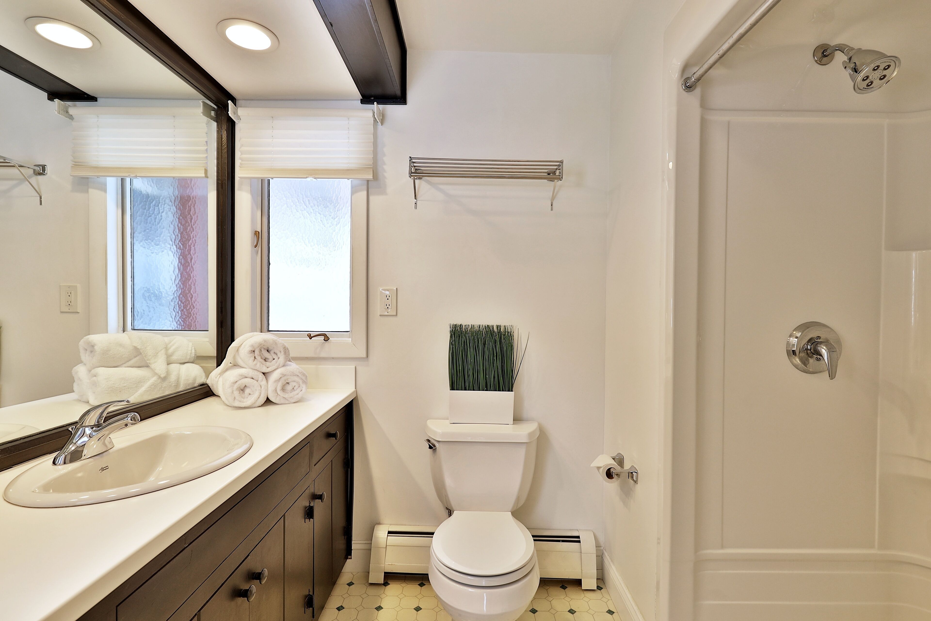 A bathroom with a white sink, toilet, and shower. There are towels on the counter and a towel rack above the toilet.