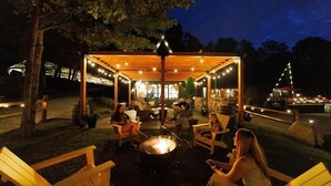 An outdoor seating area with wooden chairs and a fire pit, under a wooden pergola with string lights. - Rent An Inn! Takeover The Birch Ridge W/ Your Group. Mountain Lodge: 11 Rooms, Bar, Fireplace. 28ppl 11 Bedroom Home (Killington)