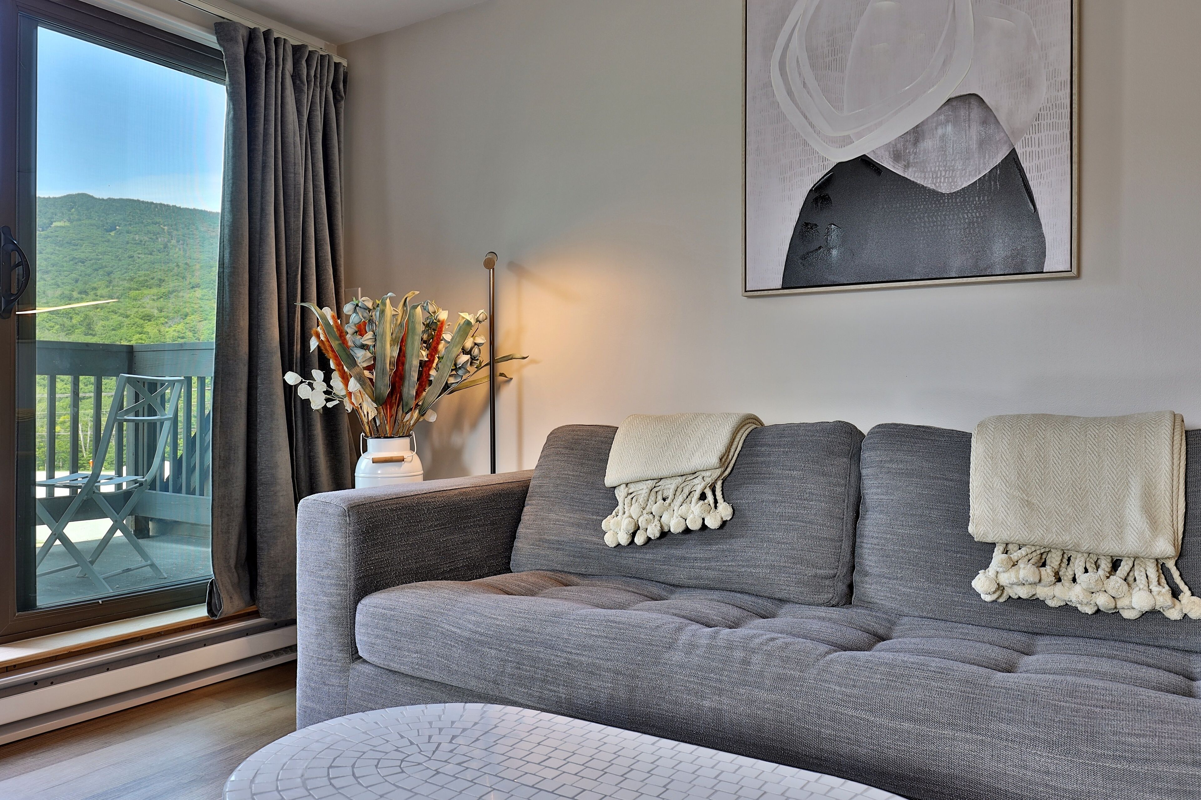 A grey sofa with a white throw blanket and a decorative vase with dried flowers.