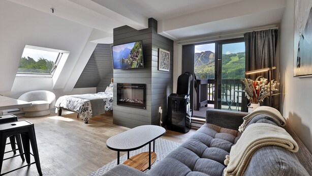 A modern loft bedroom with a large window, a fireplace, and a balcony with a scenic view.