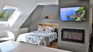 A modern bedroom with a sloped ceiling, a large bed with floral bedding, a mounted TV, and a fireplace.