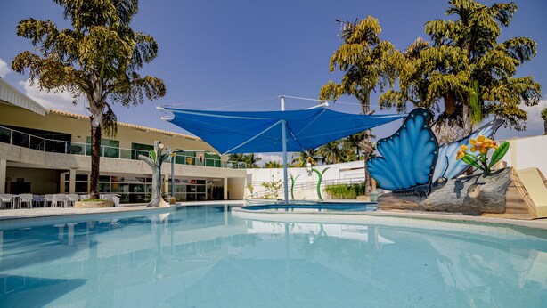 A swimming pool with a blue canopy, surrounded by palm trees and a building with a balcony. - diRoma Resort com um dia no Acqua Park (Caldas Novas)