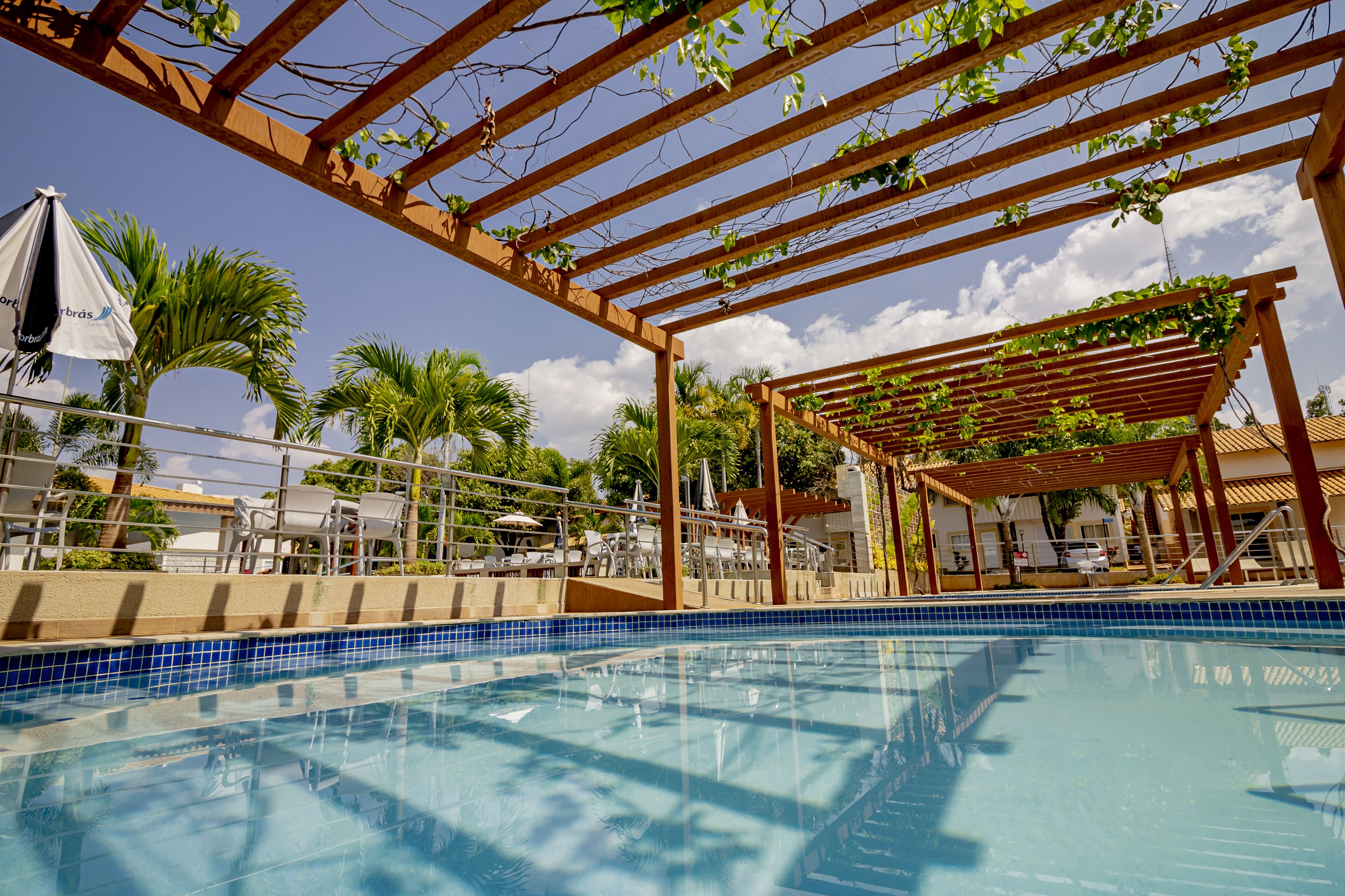 A clear blue pool with wooden pergolas and palm trees in the background.