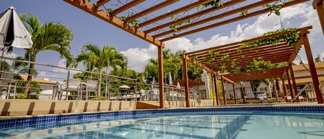 A clear blue pool with wooden pergolas and palm trees in the background.