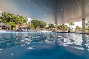 A swimming pool with a tiled edge, surrounded by palm trees and a covered area with columns. - diRoma Resort com um dia no Acqua Park (Caldas Novas)