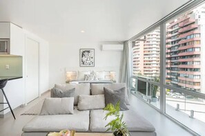 Uma sala de estar moderna com um sofá grande, uma mesa de jantar e vista para um arranha-céu.