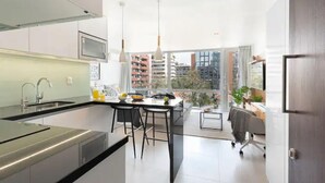 A modern kitchen with a dining area, large windows, and a view of the city. - New apartment in Barrio El Golf (Las Condes)
