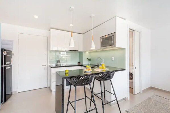 Uma cozinha moderna com uma ilha central, banquetas, micro-ondas e luminárias pendentes.