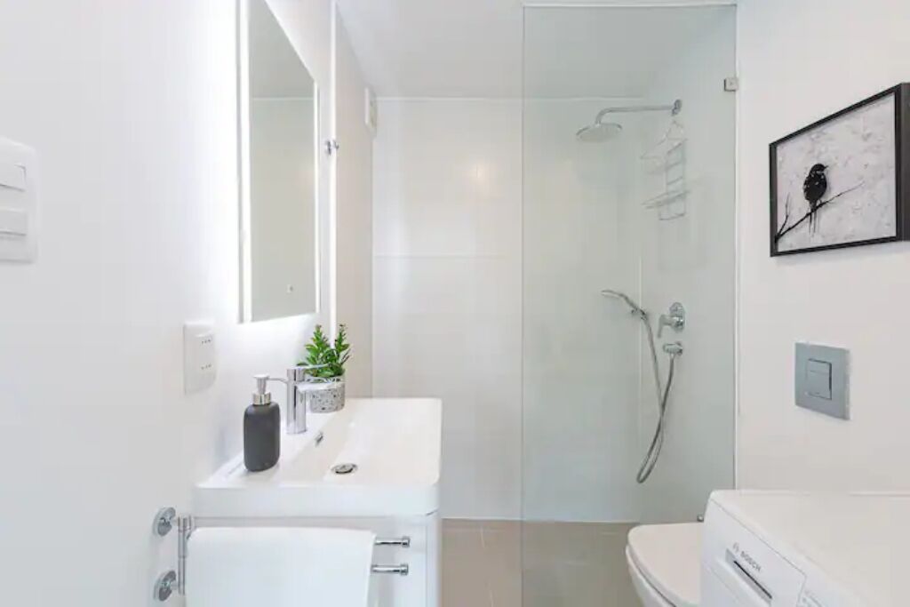 Une salle de bain moderne avec une douche à parois de verre, un lavabo blanc agrémenté d’une plante et des toilettes de la marque Bosch.