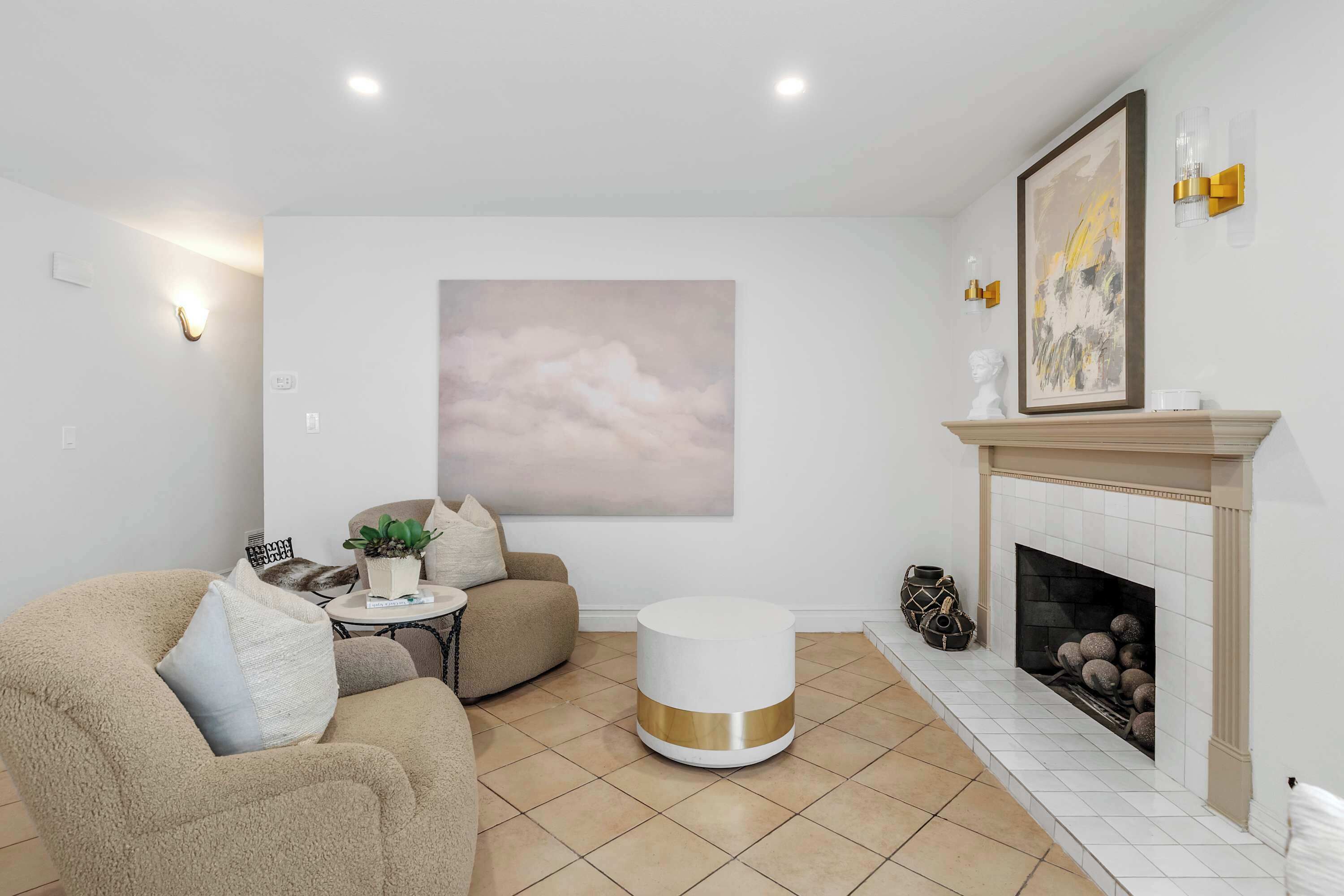 A living room with a fireplace, a round white coffee table, a beige sofa, and a large abstract painting on the wall.