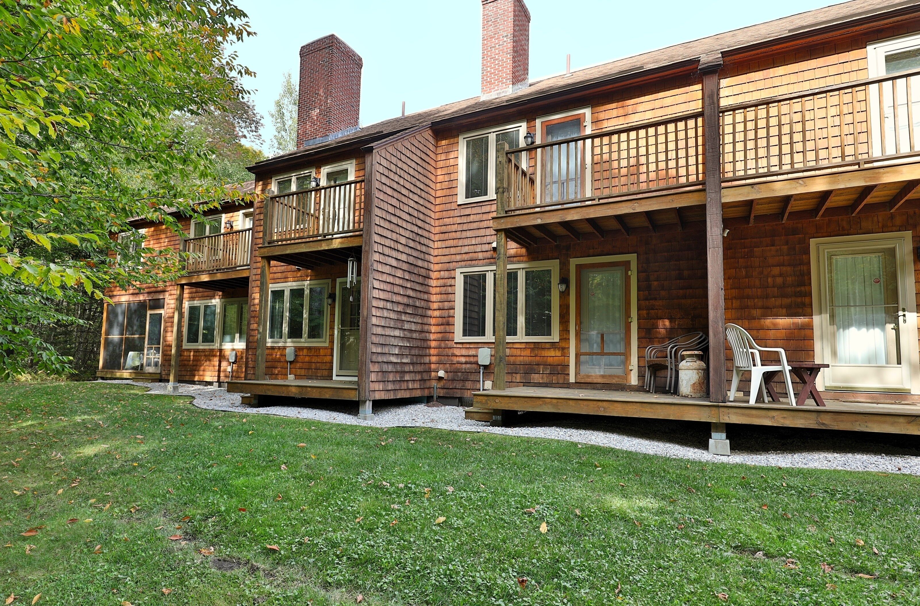 A two-story wooden house with balconies, a porch with outdoor furniture, and a well-maintained lawn.