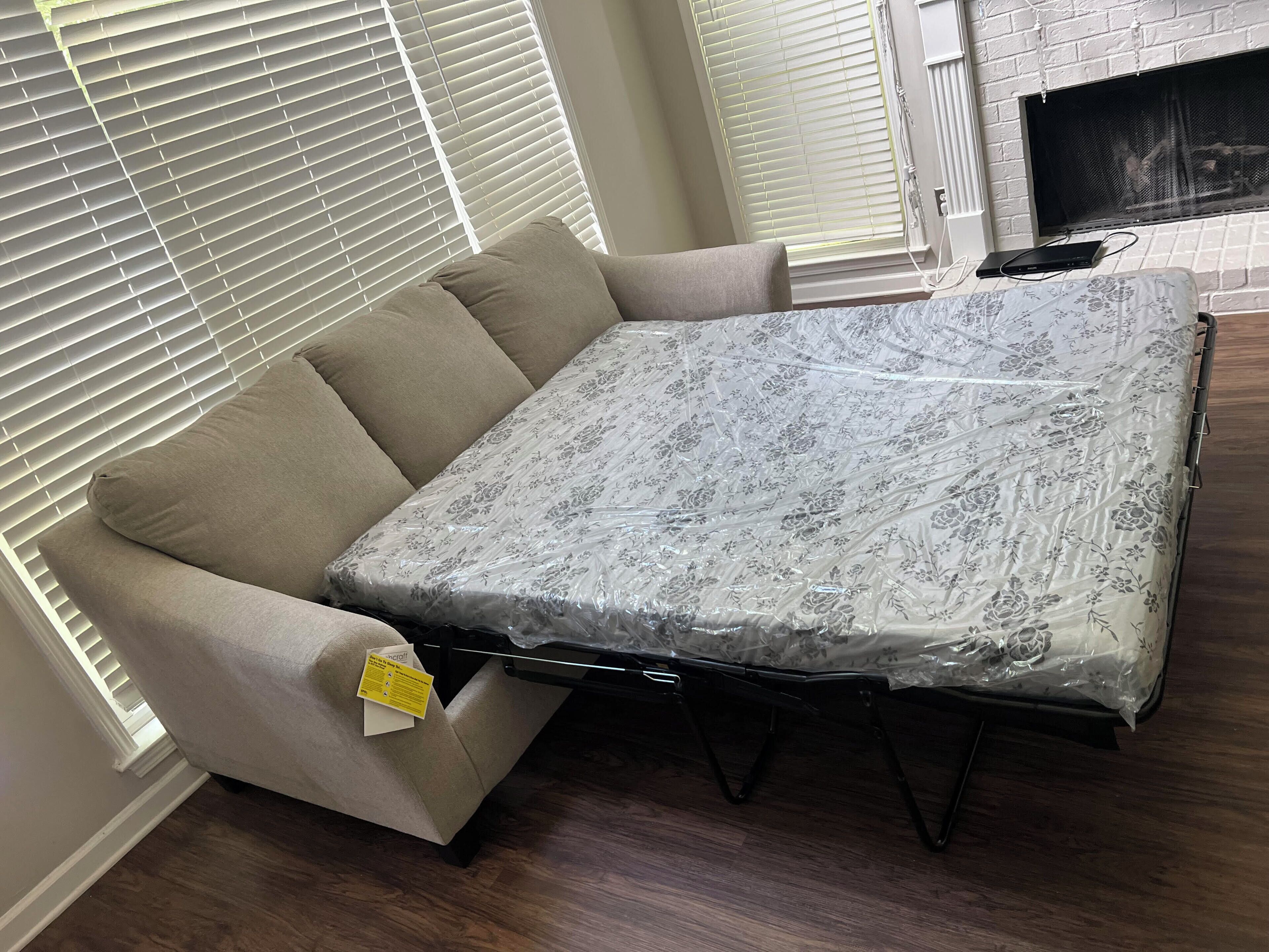 A convertible sofa with a floral-patterned cover, positioned in front of a fireplace with a white brick wall and a screen.