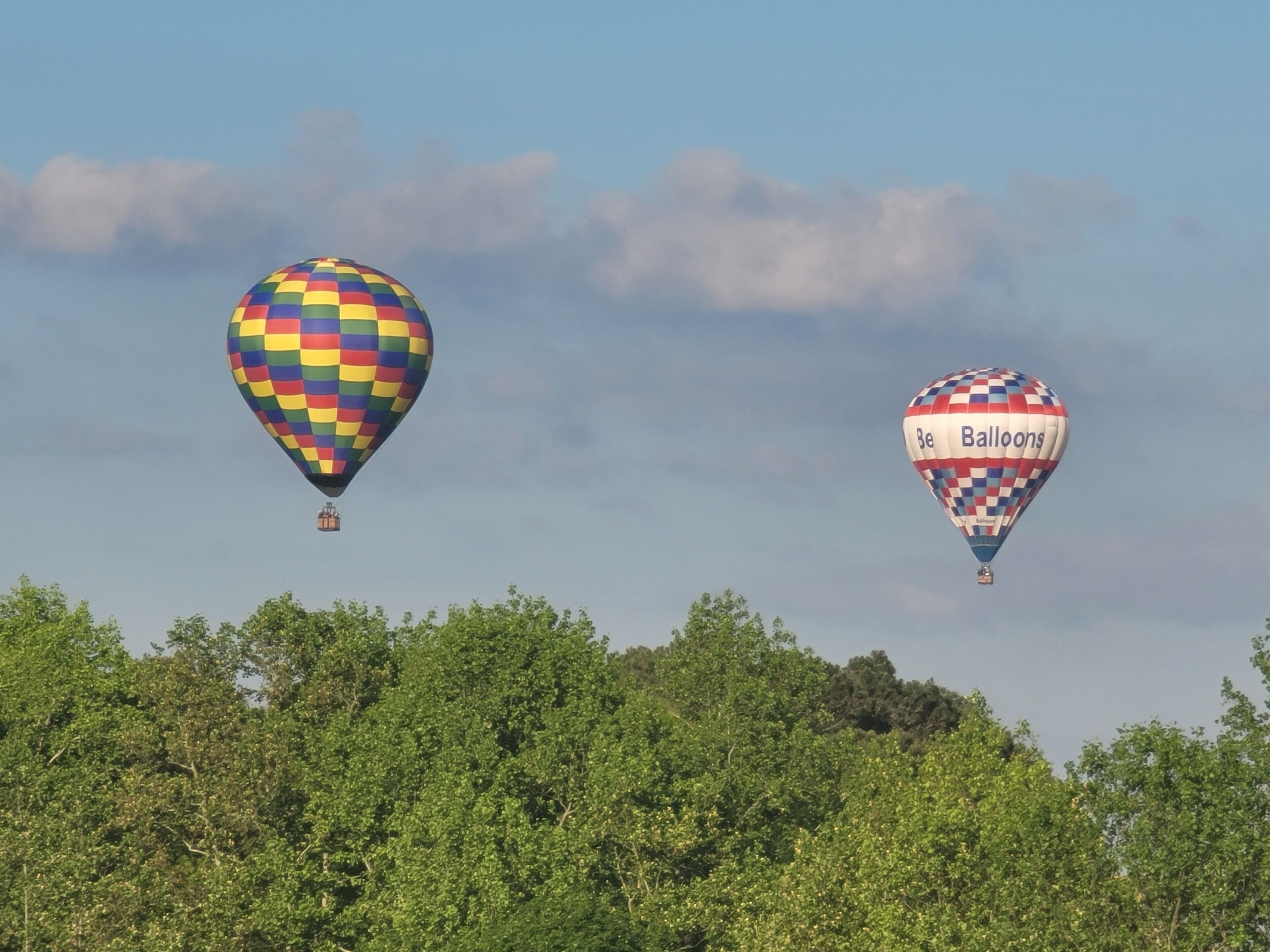 Two hot air balloons flying over a forested area.