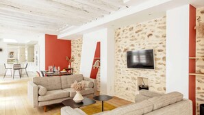 A modern living room with a sofa, coffee table, and a flat-screen TV mounted on a stone-patterned wall. - Géranimus 199 : Art of Paris (Paris)
