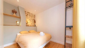 A bedroom with a bed, a wooden floor, a wall-mounted shelf with a plant, and a wall with a textured pattern. - Géranimus 199 : Art of Paris (Paris)